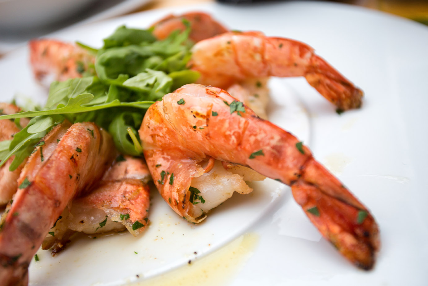 Large sautéed shrimp displayed with asian greens on a white plate.